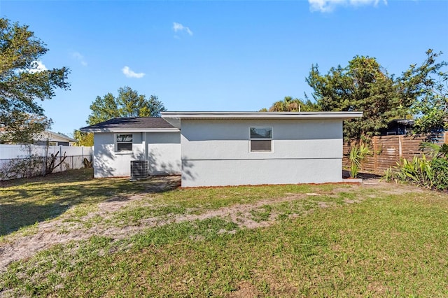 back of house with a fenced backyard, a yard, central AC unit, and stucco siding