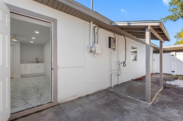 view of property exterior featuring stucco siding, a gate, a patio area, a sink, and fence