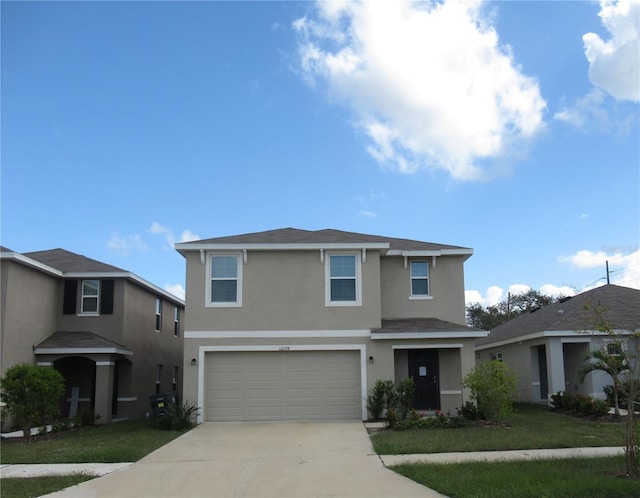 traditional-style home featuring a garage, a front yard, concrete driveway, and stucco siding