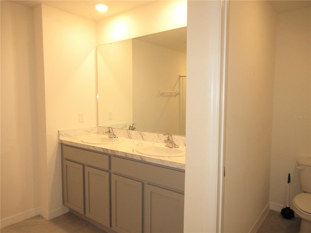 bathroom featuring toilet, double vanity, baseboards, and a sink