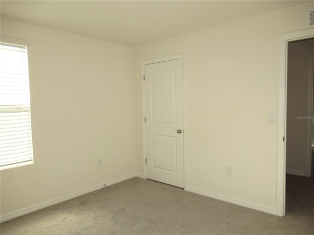 spare room with light colored carpet, visible vents, and baseboards