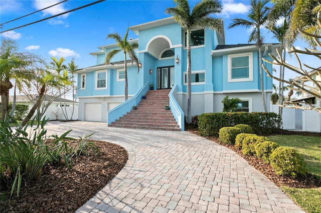 view of front facade featuring stairway, fence, decorative driveway, and stucco siding