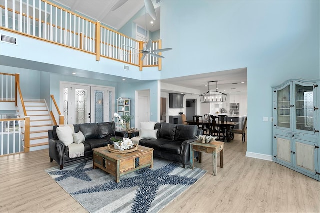 living room featuring a high ceiling, visible vents, light wood-style floors, french doors, and stairway