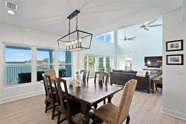 dining area featuring ceiling fan with notable chandelier, a high ceiling, visible vents, baseboards, and light wood-type flooring