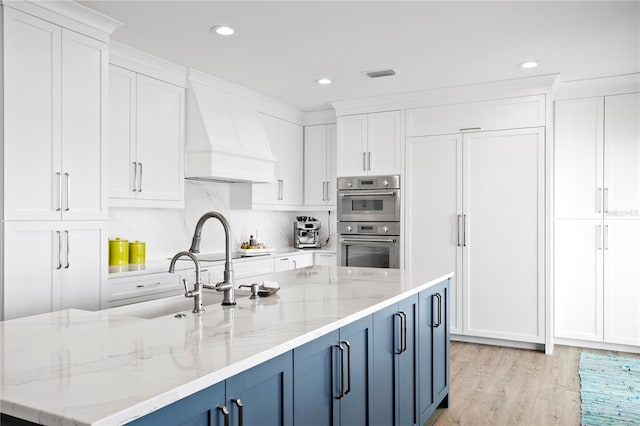 kitchen featuring premium range hood, stainless steel double oven, white cabinetry, and blue cabinets