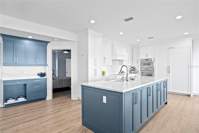 kitchen featuring custom range hood, visible vents, stainless steel double oven, a sink, and blue cabinets