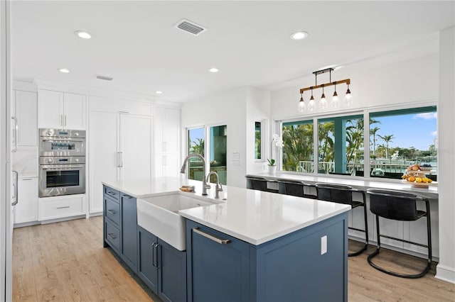 kitchen with blue cabinetry, visible vents, double oven, white cabinetry, and a sink