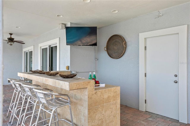 kitchen featuring brick floor, a textured wall, and ceiling fan