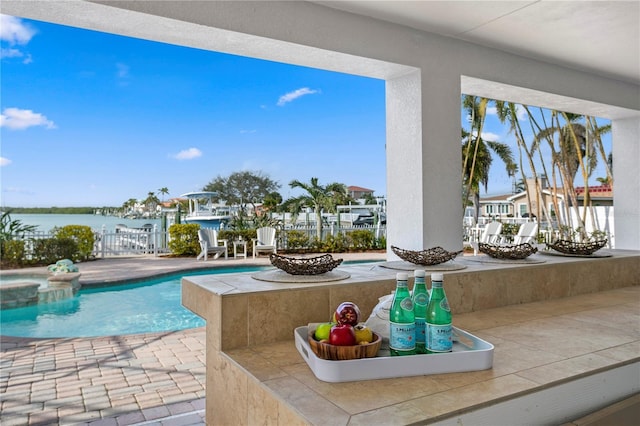 view of pool featuring a pool with connected hot tub, a water view, a patio area, fence, and a fire pit