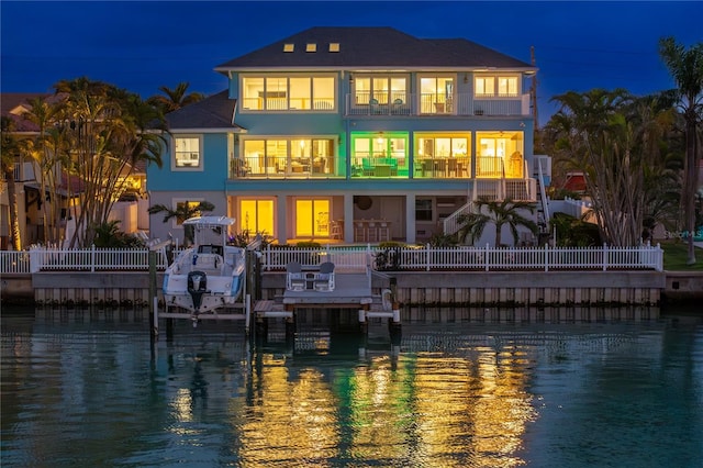 back of house at night featuring a water view, boat lift, a balcony, and stucco siding