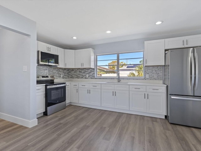 kitchen with light countertops, appliances with stainless steel finishes, light wood-style floors, white cabinetry, and a sink