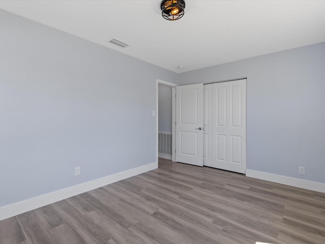 unfurnished bedroom with baseboards, a closet, visible vents, and wood finished floors