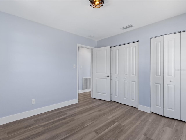 unfurnished bedroom with multiple closets, visible vents, baseboards, and wood finished floors