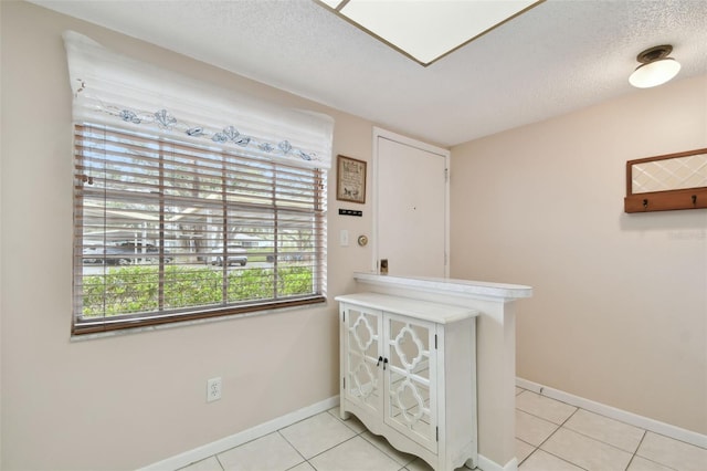 interior space featuring a textured ceiling, baseboards, and light tile patterned floors