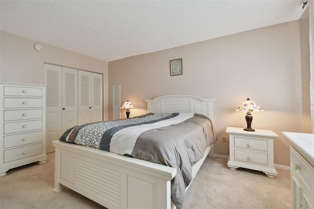 bedroom with a closet, light colored carpet, a textured ceiling, and baseboards