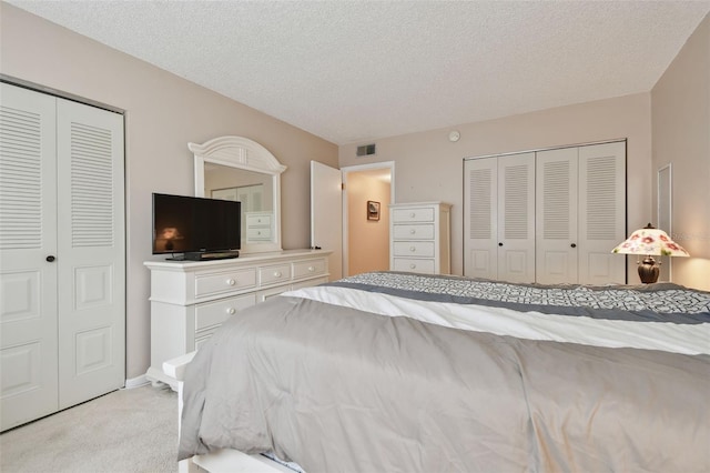 bedroom featuring multiple closets, visible vents, a textured ceiling, and light colored carpet