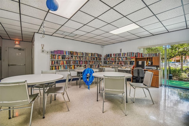 home office featuring bookshelves, a drop ceiling, and speckled floor