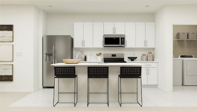 kitchen with appliances with stainless steel finishes, washing machine and dryer, a breakfast bar, and white cabinetry