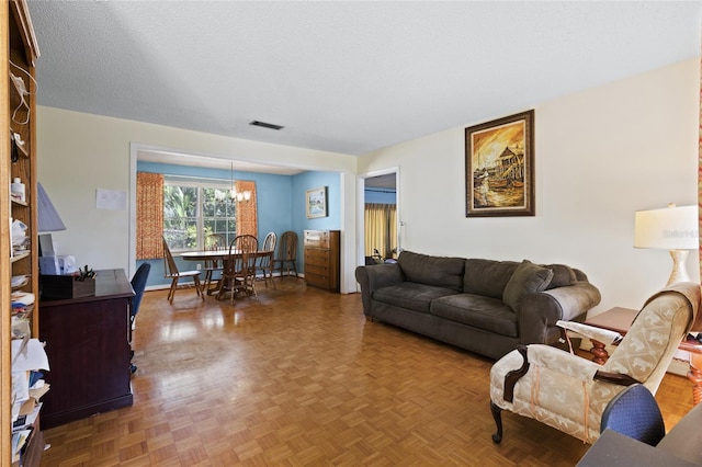 living area featuring a textured ceiling, a chandelier, visible vents, and baseboards