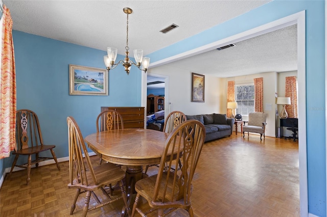 dining area with a textured ceiling, baseboards, visible vents, and a notable chandelier