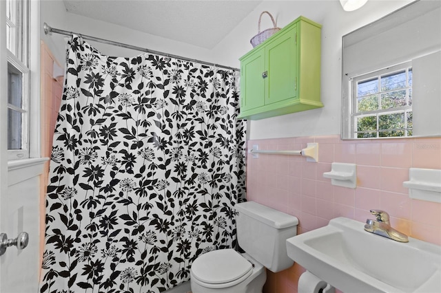 full bath featuring toilet, a wainscoted wall, a shower with shower curtain, a sink, and tile walls