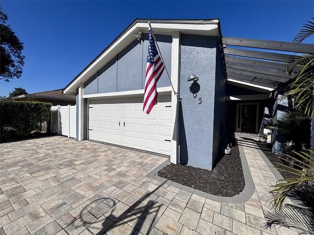 view of home's exterior with decorative driveway, fence, a garage, and stucco siding