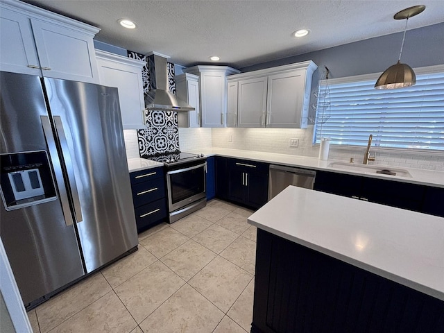 kitchen with decorative light fixtures, light countertops, appliances with stainless steel finishes, wall chimney exhaust hood, and a sink