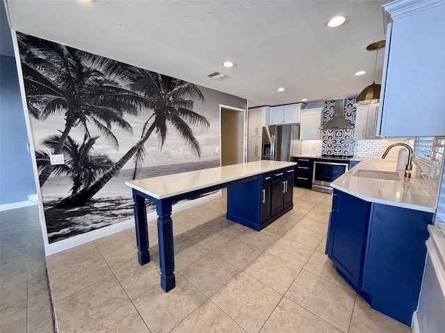 kitchen with visible vents, a sink, appliances with stainless steel finishes, wall chimney range hood, and blue cabinets