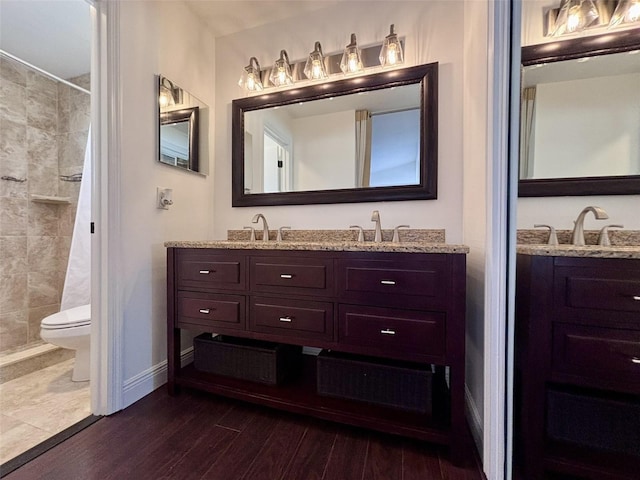 bathroom with baseboards, toilet, a tile shower, wood finished floors, and vanity