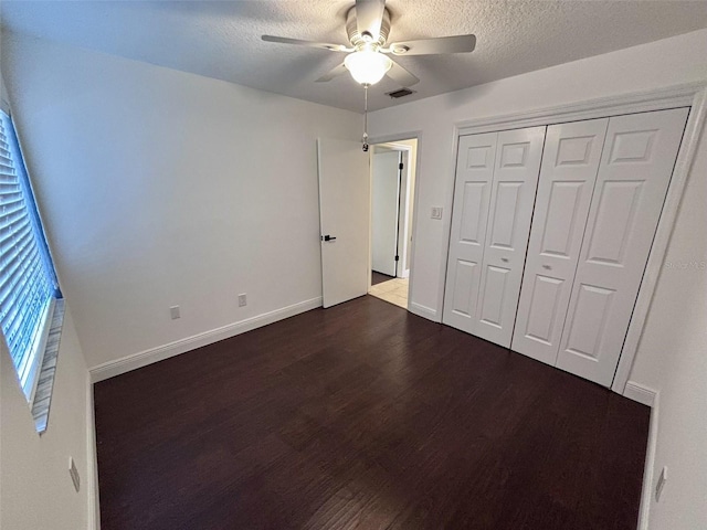 unfurnished bedroom featuring visible vents, a textured ceiling, baseboards, and dark wood-style flooring