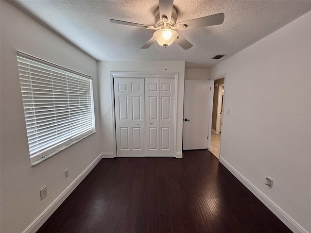 unfurnished bedroom with visible vents, baseboards, a closet, a textured ceiling, and dark wood-style flooring