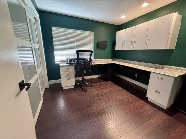 home office with baseboards, built in desk, dark wood-style flooring, and a textured ceiling