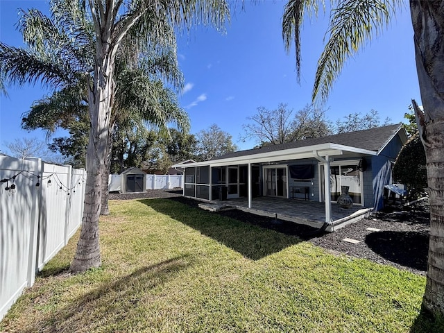 rear view of property with a storage unit, a yard, a fenced backyard, and a sunroom