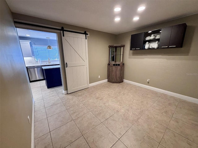 empty room featuring baseboards, a barn door, light tile patterned floors, recessed lighting, and a sink