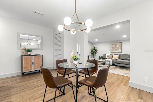 dining area with baseboards, light wood finished floors, visible vents, and a notable chandelier