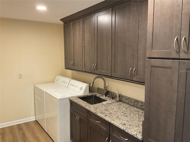 washroom featuring washing machine and dryer, a sink, baseboards, light wood-type flooring, and cabinet space