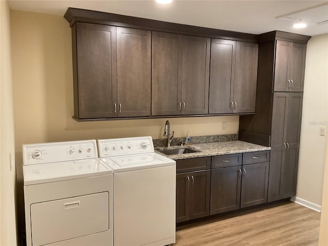 laundry room with light wood-style flooring, a sink, baseboards, cabinet space, and washing machine and clothes dryer