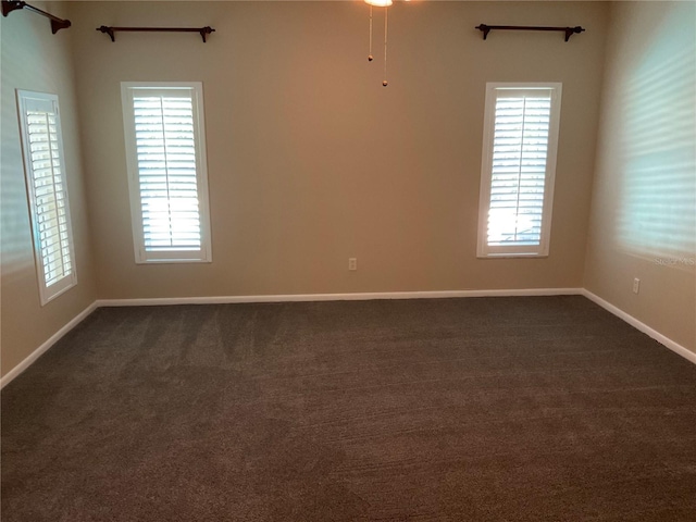 unfurnished room with baseboards and dark carpet