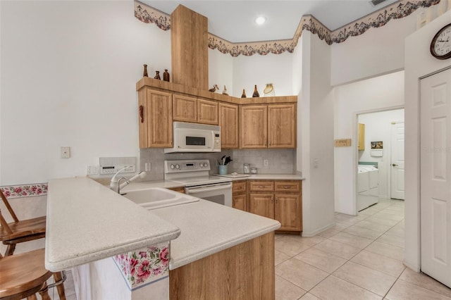 kitchen with white appliances, washer and clothes dryer, a peninsula, light countertops, and a sink