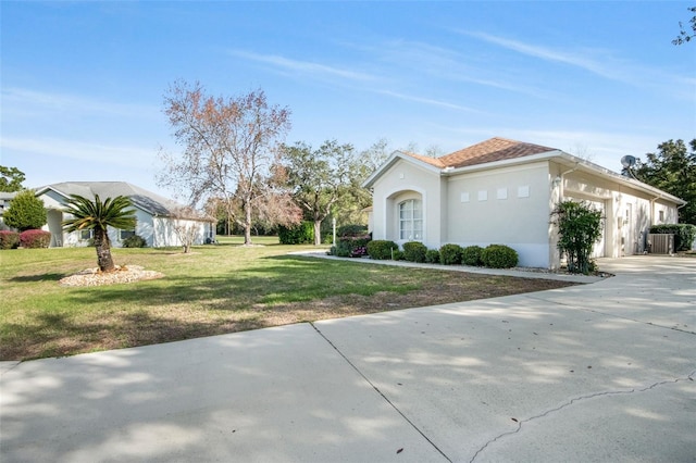 view of side of property featuring a yard, stucco siding, an attached garage, central AC unit, and driveway