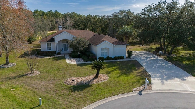 mediterranean / spanish house with a front yard, driveway, a forest view, and stucco siding