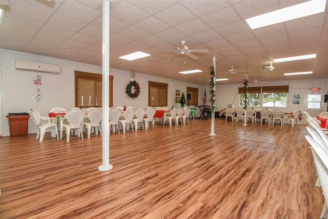 interior space featuring ceiling fan, an AC wall unit, a paneled ceiling, and light wood-style floors