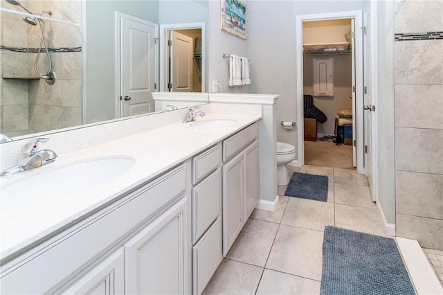 bathroom featuring toilet, double vanity, tiled shower, tile patterned floors, and a sink