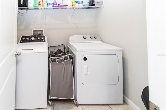 clothes washing area featuring washer and dryer, laundry area, light tile patterned floors, and baseboards