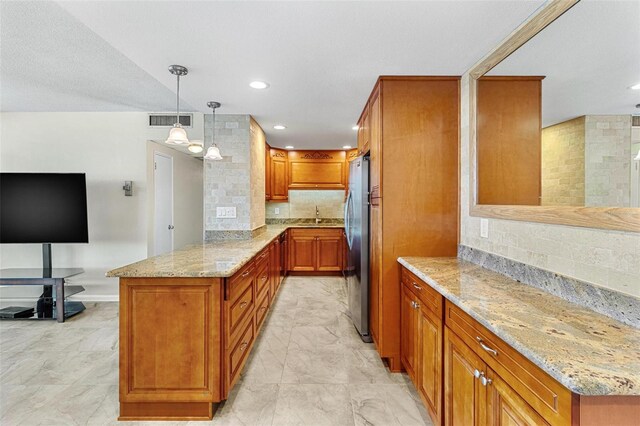 kitchen featuring visible vents, freestanding refrigerator, a peninsula, brown cabinetry, and light stone countertops