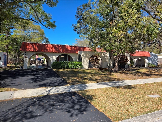 mediterranean / spanish-style home featuring aphalt driveway, stucco siding, a tiled roof, and a front yard