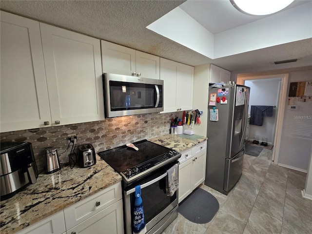 kitchen featuring light stone counters, decorative backsplash, white cabinets, appliances with stainless steel finishes, and a textured ceiling