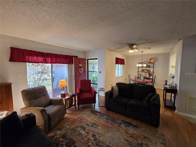 living area featuring visible vents, baseboards, ceiling fan, wood finished floors, and a textured ceiling