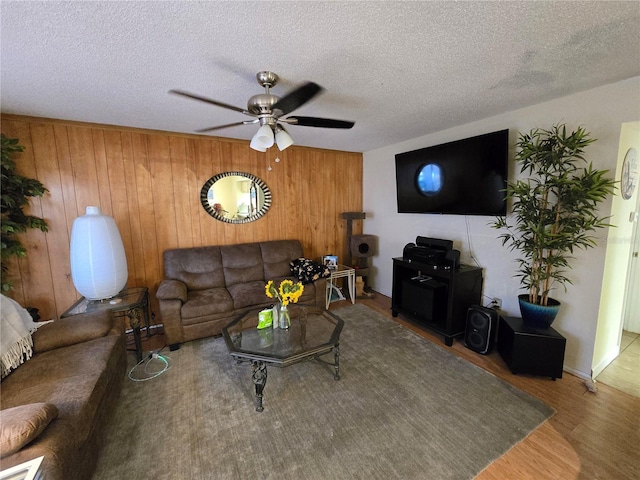 living area featuring wooden walls, a textured ceiling, wood finished floors, and a ceiling fan