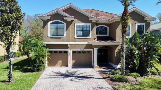 mediterranean / spanish house with stucco siding, a tile roof, decorative driveway, a front yard, and a garage